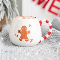 a white mug with a gingerbread design on it sitting next to a christmas tree