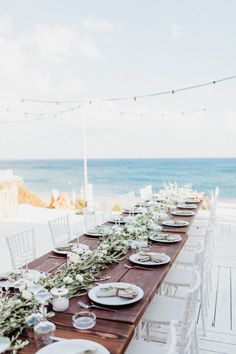 a long table set with plates and place settings for an outdoor dinner on the beach