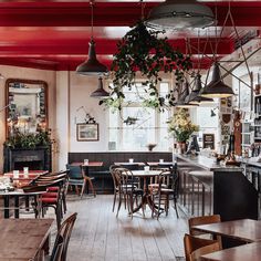 the interior of a restaurant with tables, chairs and plants hanging from the ceiling above