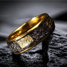 a gold wedding ring sitting on top of a black rock in front of a dark background