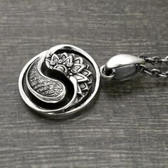 a silver pendant with a flower on the bottom and a yin symbol in the middle