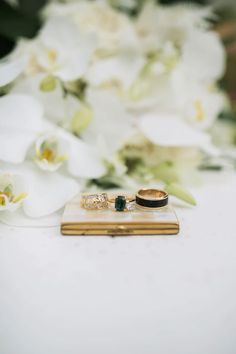 two wedding rings sitting on top of a book next to white flowers and orchids