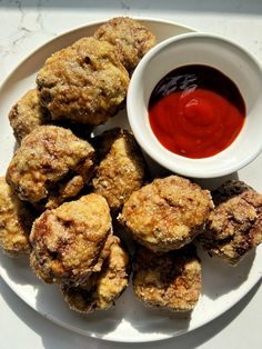 some fried food on a white plate with ketchup and sauce in a bowl