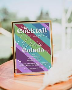 a colorful cocktail party sign on a wooden table with white feathers in the foreground