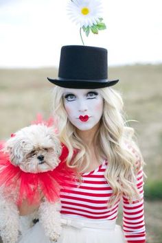 a woman with white makeup holding a dog wearing a top hat and red bow tie