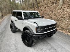 a white truck parked on the side of a dirt road in front of some trees