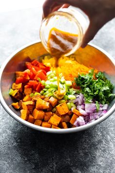 a person pouring dressing into a bowl filled with chopped veggies and other ingredients