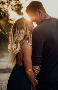 a man and woman standing next to each other with the sun shining through trees behind them