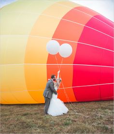 a bride and groom standing in front of a large hot air balloon with balloons attached to it