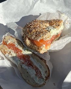 two bagels with meat, cheese and tomato on them are sitting on wax paper