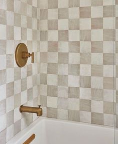 a bath tub sitting next to a wall with checkered tile on the back splash