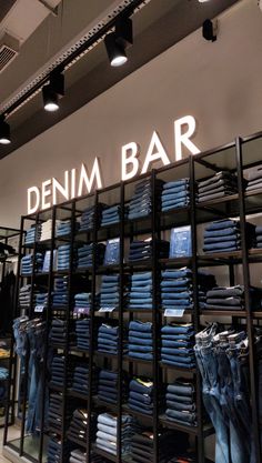 the inside of a clothing store with clothes on racks and neon sign above it that says denim bar