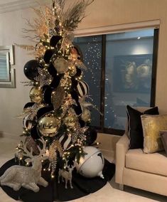 a christmas tree decorated with black and gold ornaments in a living room area next to a couch