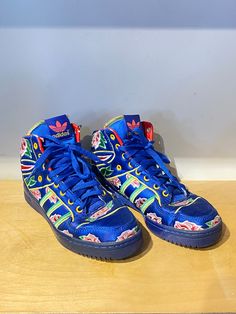 Adidas x Jeremy Scott Blue Floral High Tops! These eye catching sneakers feature a blue satin base with colorful embroidered flowers throughout. They are marked a Men's Size 7.5 and are in overall excellent condition with minor wear to the leather at the ankle, priced as is. Approx. Measurements: Width: 3.5" Heel to toe: 10" Sporty Floral Print Sneakers With Round Toe, Spring Blue High-top Sneakers With Rubber Sole, Floral Print High-top Sneakers For Streetwear, Blue Sporty High-top Sneakers For Spring, Sporty Blue High-top Sneakers For Spring, Sporty Floral Print Sneakers For Streetwear, Blue High-top Sneakers With Round Toe For Spring, Blue High-top Sneakers For Spring, Blue Lace-up High-top Sneakers For Spring