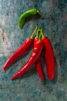 three red chili peppers on a blue surface with one green pepper in the foreground