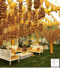 an outdoor wedding venue with lots of yellow flowers hanging from the ceiling and white couches