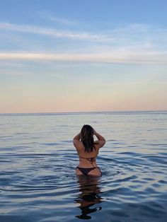 a woman is sitting in the water with her back to the camera and looking at the horizon