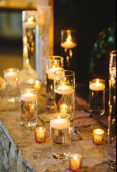 many lit candles are lined up on a stone ledge in front of some glass vases