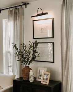 two vases with plants sit on a table in front of a window and framed pictures