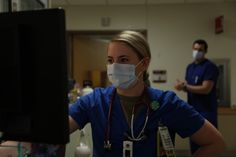 a nurse wearing a face mask in front of a computer screen while another doctor looks on