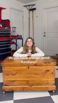 a woman sitting on top of a wooden trunk in a garage with the words do you have orange wood furniture?