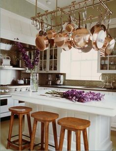 a kitchen with pots and pans hanging from the ceiling, two stools in front of an island