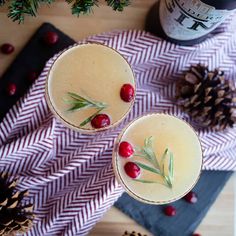 two glasses filled with drinks sitting on top of a wooden table next to pine cones