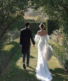 a bride and groom walking down a path holding hands