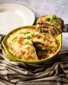 a piece of pizza is being lifted from a green casserole dish on a striped cloth