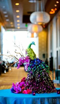 a peacock statue sitting on top of a table next to a blue cloth covered table