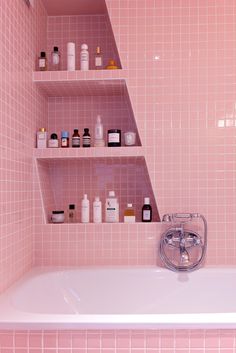 a pink tiled bathroom with shelves above the bathtub