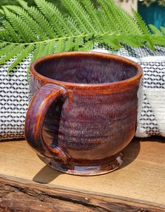 a coffee cup sitting on top of a wooden table next to a fern leaf pillow