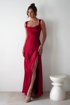 This gown is your perfect choice for debs, prom or any formal event. A look that blends classic glamour with contemporary style. Designed for timeless allure and effortless sophistication. Featuring a graceful cowl neckline and thick shoulder straps, this dress offers a flattering, structured fit. The sultry thigh-high slit adds a bold, modern touch, while the luxurious satin fabric drapes beautifully to enhance your silhouette. Highlights Stunning red gown with cowl neckline Soft satin material Red Fitted Floor-length Satin Dress, Red Fitted Backless Satin Dress, Red Fitted Satin Dress For Prom, Satin Maxi Dress With Lace-up Back For Prom, Red Fitted Satin Maxi Dress, Formal Satin Dress With Cowl Back, Fitted Satin Finish Evening Dress With Cowl Back, Fitted Floor-length Satin Dress With Back Opening, Satin Gown With Corset Back And Maxi Length