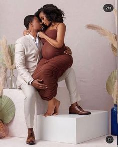 a man and woman are hugging each other while standing on a white pedestal with plants in the background