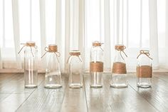 five empty glass bottles with rope tied around them on the floor in front of a window