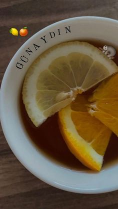 a bowl filled with liquid and sliced lemons on top of a wooden table next to an orange slice