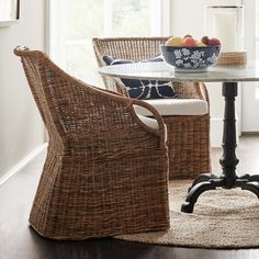 a wicker chair sits next to a table with fruit on it in front of a window