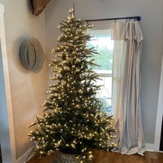 a small christmas tree in a pot on the floor next to a window with curtains