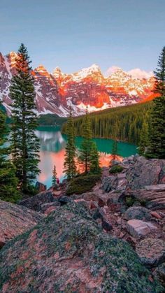 the mountains are covered in snow and pine trees, with a lake surrounded by rocks