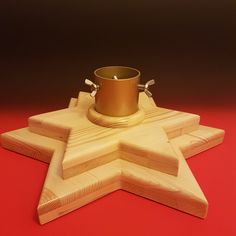 a wooden star shaped candle holder with a gold cup in the center on a red background