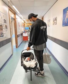 a man holding a baby in a stroller while walking down a hallway with posters on the walls