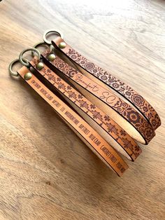 four leather key chains with engraved names on them sitting on a table next to a cell phone