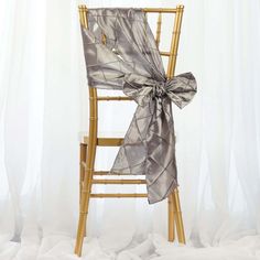 a chair with a bow tied to it sitting in front of a white curtained background