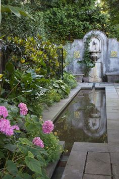 a garden with water and flowers in the foreground, surrounded by greenery on either side