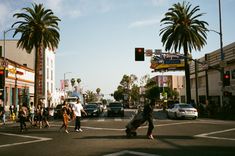 people crossing the street at an intersection with palm trees