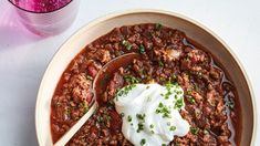 a bowl of chili with sour cream on top and a glass of water next to it