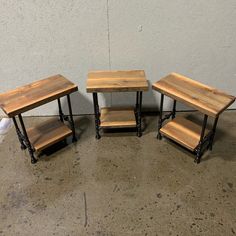 three wooden tables sitting next to each other on top of a cement floor in front of a white wall