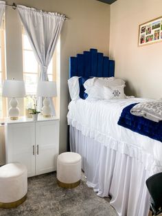 a white bed with blue headboard and foot stools in a bedroom next to a window