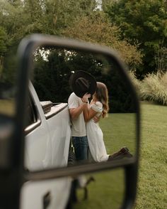 a man and woman standing in front of a white truck looking at the rear view mirror