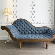 a blue chaise lounge sitting on top of a hard wood floor next to a lamp